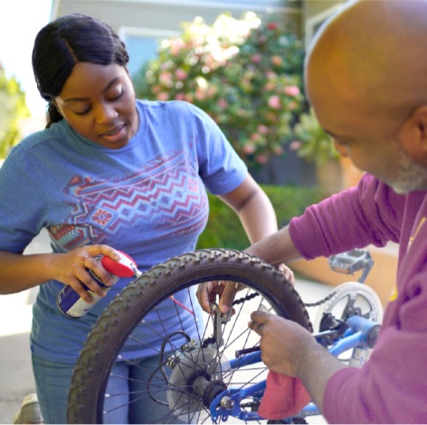 Father and daughter oiling a bicycle chain outside together