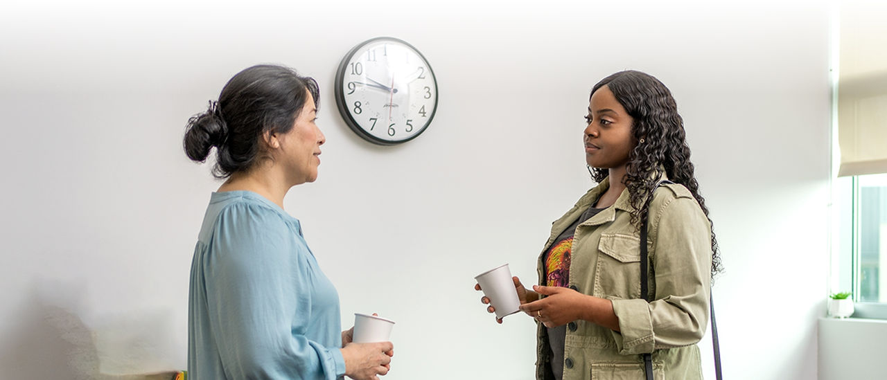 Two women chatting in front of a clock